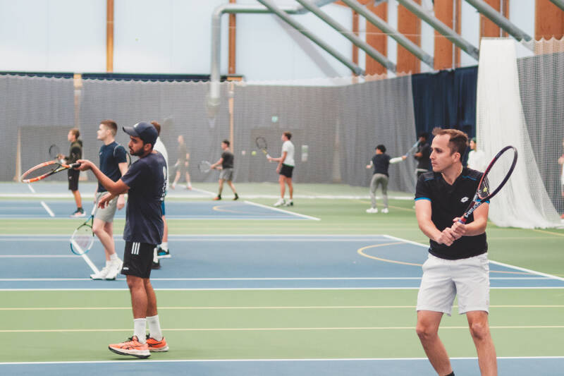 Wide photo of university students playing tennis on acrylic tennis courts
